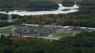 AX152_211 - 5.5K aerial stock footage flying over fall foliage toward Massachusetts Correctional Institution at Norfolk and the water, Massachusetts