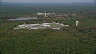 AX152_218 - 5.5K aerial stock footage of a wide view of fall foliage approaching Massachusetts Correctional Institution Cedar Junction, Walpole, Massachusetts