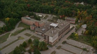 AX152_220E - 5.5K aerial stock footage orbiting away from an abandoned hospital among fall foliage, Walpole, Massachusetts