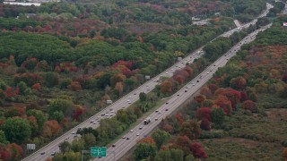 AX152_235 - 5.5K aerial stock footage flying over interstate with traffic towards trees with fall foliage, Norwood, Massachusetts