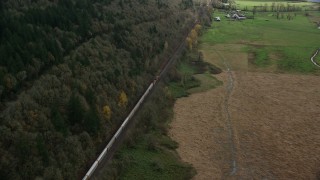 AX153_178E - 5.5K aerial stock footage approaching a train traveling by fields and water in Washougal, Washington