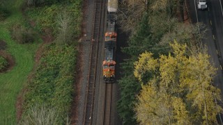 AX153_183 - 5.5K aerial stock footage of a reverse view tracking a train in Columbia River Gorge, reveal trucks on country road in Oregon