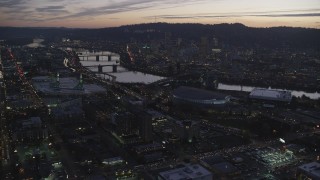 AX155_260 - 5.5K stock footage aerial video approaching Moda Center, Willamette River, and downtown skyscrapers at twilight, Downtown Portland, Oregon