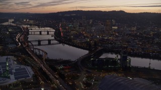 AX155_260E - 5.5K aerial stock footage flying over Moda Center, Willamette River, toward downtown skyscrapers at twilight, Downtown Portland, Oregon