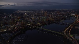 AX155_267E - 5.5K aerial stock footage flying away from KOIN Center and Downtown Portland cityscape beside the Willamette River at twilight, Oregon