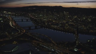 AX155_301 - 5.5K aerial stock footage crossing the Willamette River to approach Burnside Bridge, White Stag Sign, and Downtown Portland at night in Oregon