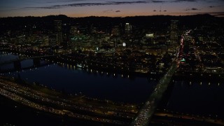 AX155_317E - 5.5K aerial stock footage of a view across the Burnside Bridge and Willamette River of Downtown Portland and the White Stag Sign, Oregon, at night
