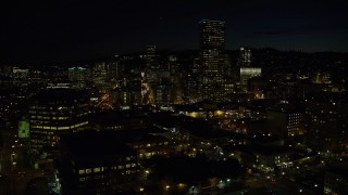 AX155_365E - 5.5K aerial stock footage approaching and passing US Bancorp Tower and skyscrapers by the Willamette River at nighttime, Downtown Portland, Oregon