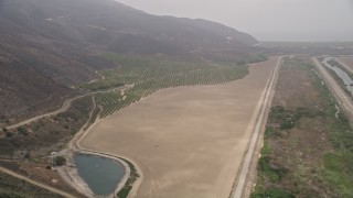 AX42_050E - 5K aerial stock footage follow a country road to approach crops and farmland in light fog, Point Mugu, California