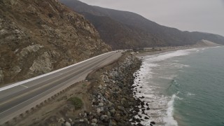 AX42_061E - 5K aerial stock footage fly low over ocean waves by Highway 1 with light traffic, Point Mugu, California