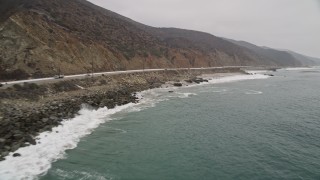 AX42_071E - 5K aerial stock footage fly low over waves crashing against the coast near Highway 1, Malibu, California