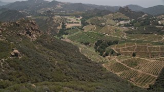 AX42_104E - 5K aerial stock footage approach and fly over rock formations to reveal hilly vineyards, Malibu, California