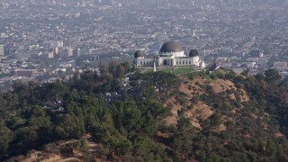AX43_011 - 4K aerial stock footage flying low over palm trees to approach and flyby the Griffith Observatory, Los Angeles California