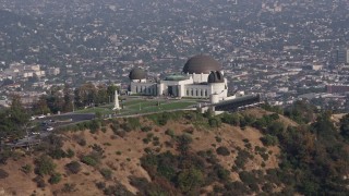 AX43_016E - 4K aerial stock footage of the Griffith Observatory seen while descending behind trees, Los Angeles