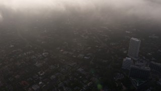 AX43_056 - 4K aerial stock footage flying over the edge of marine layer clouds and tilt down to Los Angeles below, California