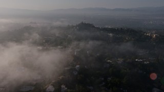 AX43_058E - 4K aerial stock footage flying over marine layer clouds to reveal hillside homes and radio tower in Beverly Hills, California