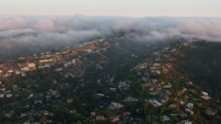 AX44_002 - 4K aerial stock footage flying by upscale, hillside homes with fog rolling over the hills, Sherman Oaks, California, sunset