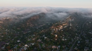 AX44_003 - 4K aerial stock footage of upscale hillside homes with fog rolling over the hills, Sherman Oaks, California, sunset