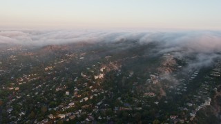 AX44_004 - 4K aerial stock footage of Hillside homes with fog rolling over the tops of hills, Sherman Oaks, California, sunset