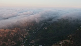 AX44_006 - 4K aerial stock footage of a marine layer pouring over the hills, Studio City, California, sunset