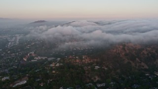 AX44_014 - 4K aerial stock footage flying over homes with marine layer flowing over hills, Studio City, California, sunset