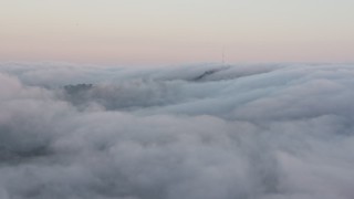 AX44_015 - 4K aerial stock footage of radio tower peaking through a marine layer, Hollywood Hills, California, sunset