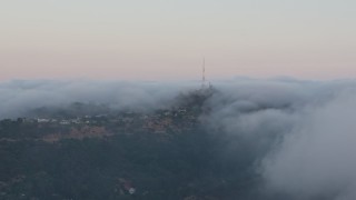 AX44_016 - 4K aerial stock footage of a radio tower peaking out from marine layer, Hollywood Hills, California, sunset