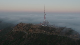AX44_022 - 4K aerial stock footage of a radio tower atop Hollywood Hills near marine layer, California, sunset