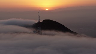 AX44_032E - 4K aerial stock footage of sun setting behind Hollywood Hills and radio tower in marine layer, California
