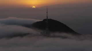 AX44_033 - 4K aerial stock footage approaching radio tower atop a hill in marine layer, Hollywood Hills, California, sunset