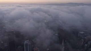 AX44_042E - 4K aerial stock footage of city covered in marine layer, Downtown Los Angeles, sunset