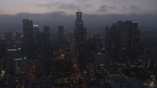 AX44_069 - 4K stock footage aerial video flying by skyscrapers under marine layer, Downtown Los Angeles, twilight