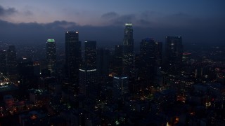 AX44_070 - 4K aerial stock footage flying by skyscrapers below marine layer, Downtown Los Angeles, twilight