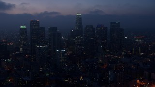 AX44_071E - 4K aerial stock footage flying by skyscrapers below marine layer, Downtown Los Angeles, twilight