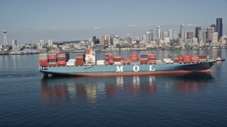 AX47_026E - 5K aerial stock footage orbit a cargo ship sailing Elliott Bay with the skyline in the background, Downtown Seattle, Washington