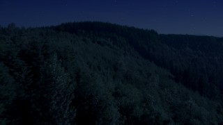AX48_083_DFN - 4K day for night color corrected aerial stock footage of flying over an evergreen forest and approach a mountain ridge in the Cascade Range, Washington