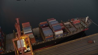 AX50_068 - 5K aerial stock footage of flying over cargo ships laden with containers docked beneath cranes at the Port of Seattle, Washington, sunset