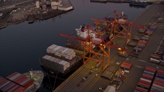 AX50_068E - 5K aerial stock footage of flying over cargo ships laden with containers docked beneath cranes at the Port of Seattle, Washington, sunset