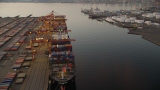 AX50_069 - 5K aerial stock footage orbit a cargo ship stacked with shipping containers beneath cranes at the Port of Seattle, Washington, sunset