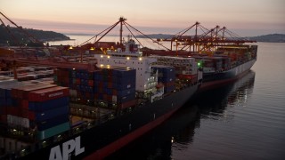 AX50_070 - 5K aerial stock footage flyby a pair of loaded cargo ships docked beneath cranes at the Port of Seattle, Washington, sunset