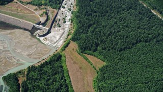 AX52_025 - 5K aerial stock footage of North Fork Toutle River beside evergreen forest, reveal a sediment retentions structure dam, Washington