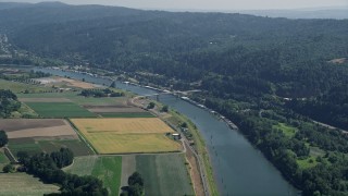 AX52_104E - 5K aerial stock footage of a bridge spanning Multnomah Channel by crop fields in Riverview, Oregon
