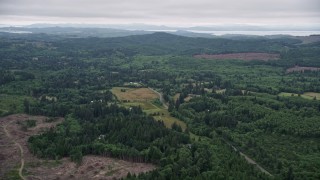 AX56_062 - 5K aerial stock footage of a farm field beside a country road, evergreen forest, and clear cut areas in Clatsop County, Oregon