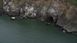 AX56_100 - 5K aerial stock footage of sea cave at the base of a cliff in Cape Disappointment, Washington