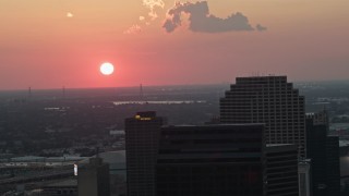 AX61_071 - 5K aerial stock footage of the setting sun behind Plaza Tower and Downtown New Orleans, Louisiana