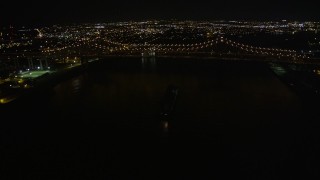 AX62_015 - Aerial stock footage of 5K aerial  video of cargo ship sailing under Crescent City Connection Bridge at night, New Orleans, Louisiana
