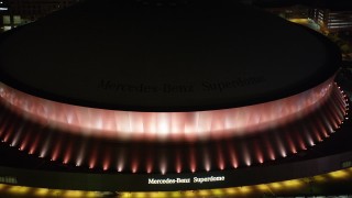 AX63_023 - 5K aerial stock footage of Mercedes-Benz Superdome with orange lighting at night, Downtown New Orleans, Louisiana