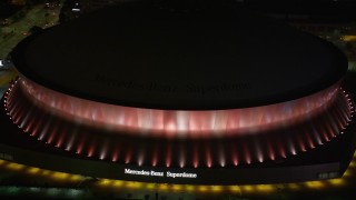 AX63_023E - 5K aerial stock footage of Mercedes-Benz Superdome with orange lighting at night, Downtown New Orleans, Louisiana