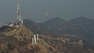 AX64_0014E - 5K aerial stock footage of emergency helicopter flying around Hollywood Sign and landing by the radio towers, Los Angeles, California