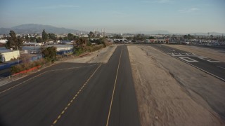 AX64_0047E - 5K aerial stock footage of lifting off from the runway at Whiteman Airport, fly over homes and warehouse buildings, Pacoima, California